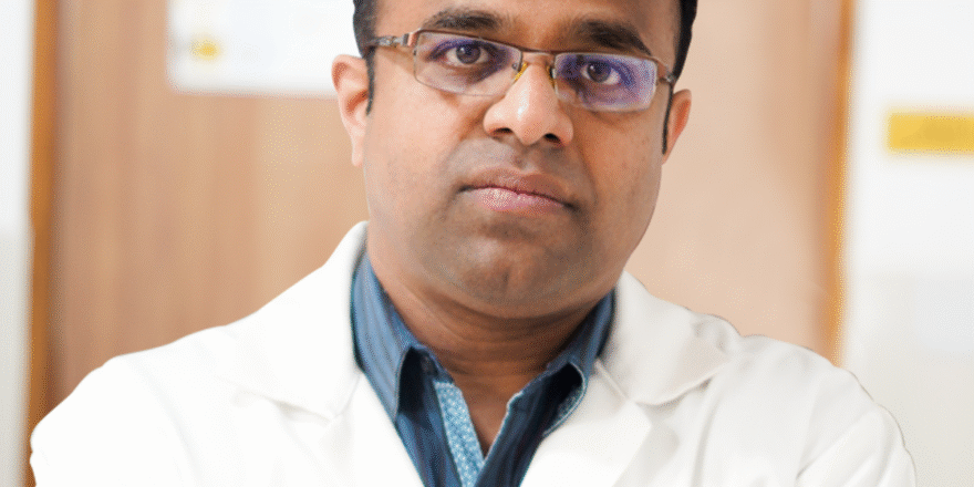 Dr. Tejaswi M. in a white coat with arms crossed, looking directly at the camera.